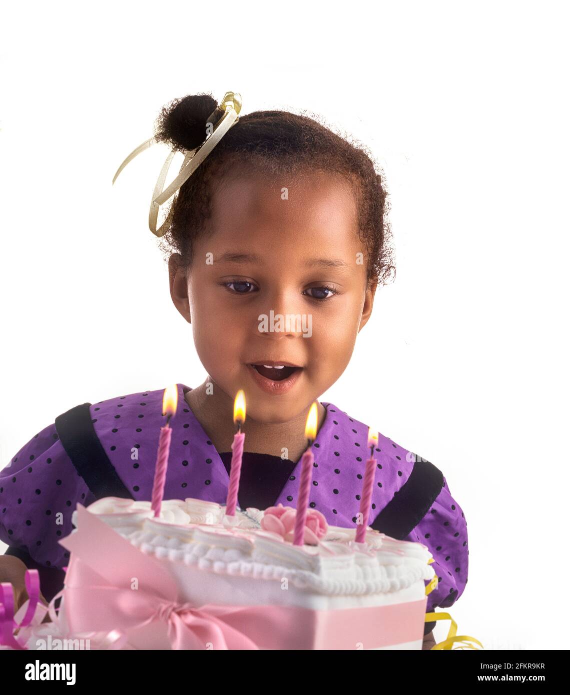 Candele per torta di compleanno INFANTILE 4 anni graziosa ragazza britannica afro-caraibica che festeggia con la sua speciale torta di compleanno e che esprime il desiderio di far saltare in aria le quattro candele, sfondo bianco ritaglio Foto Stock