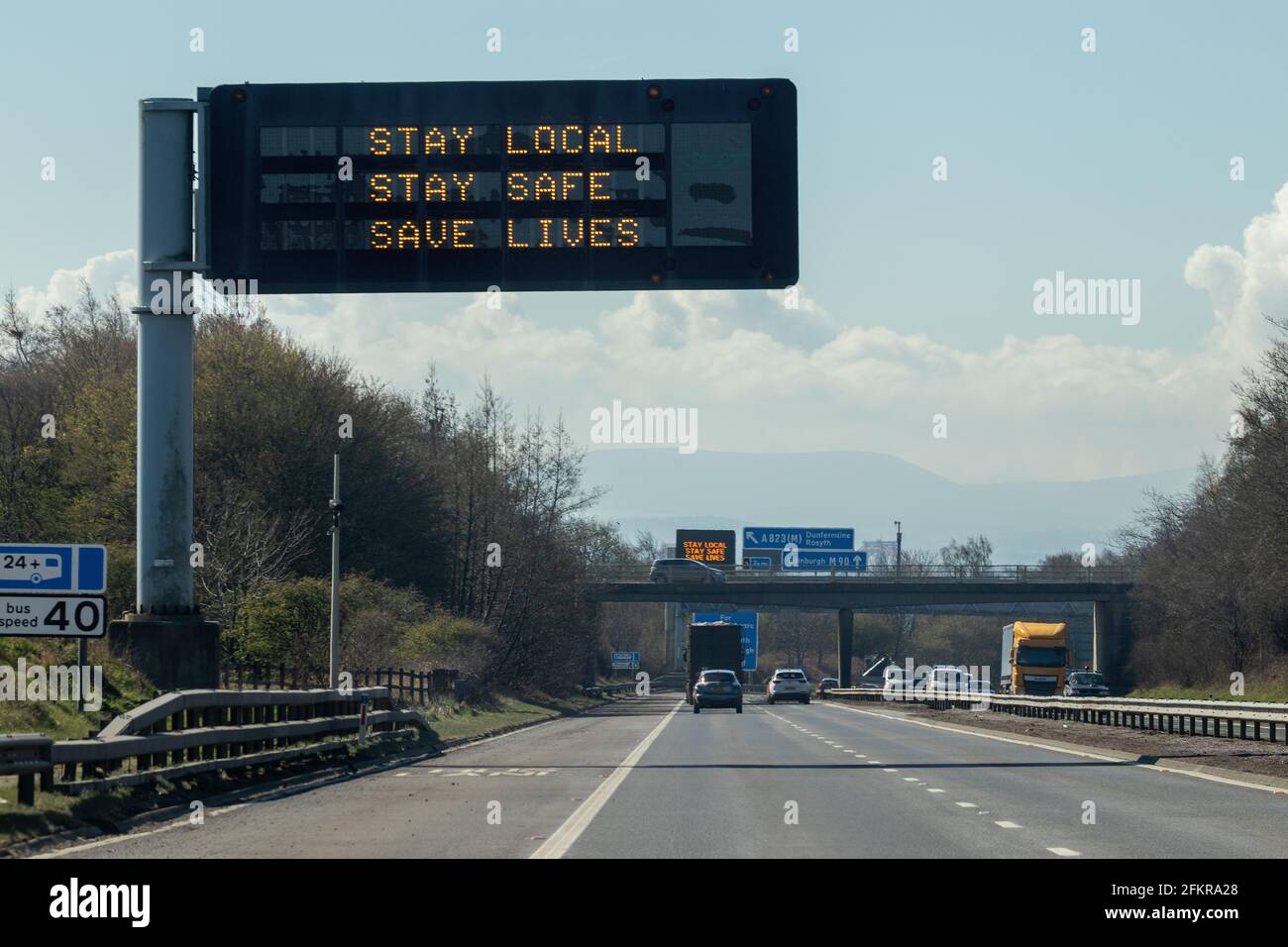 Un cartello autostradale in Scozia che dice soggiorno locale, soggiorno sicuro, salvare vite Foto Stock