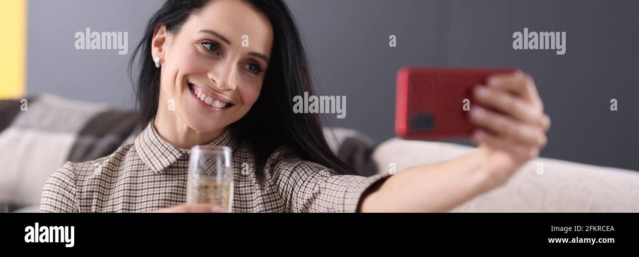 Donna sorridente che tiene un bicchiere di champagne e guarda lo smartphone schermo Foto Stock