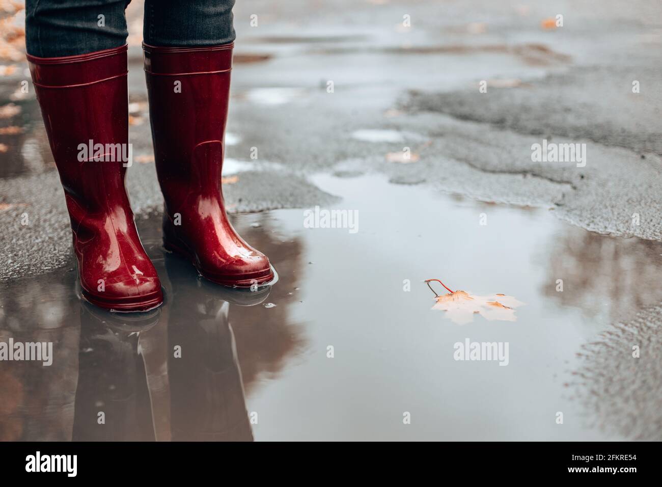I piedi femmina in gomma rossa stivali in piedi in un fangoso puddle sotto la pioggia nel tempo di autunno Foto Stock