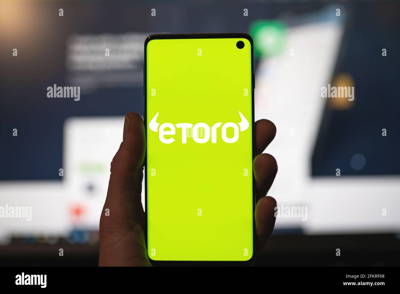 Uomo che tiene uno smartphone con il logo Etoro con sito web sfocato come sfondo. Piattaforma di trading, investendo in azioni e criptovalute Foto Stock