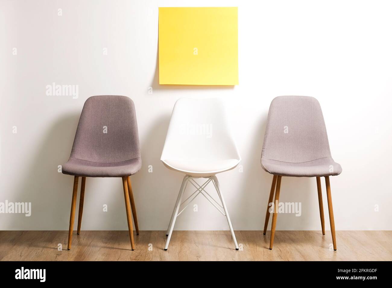 Tre poltrone in stile loft vuote disponibili su pavimento in legno con poster vuoto, sfondo bianco sulla parete, adesivo giallo per il testo. Intervie Foto Stock