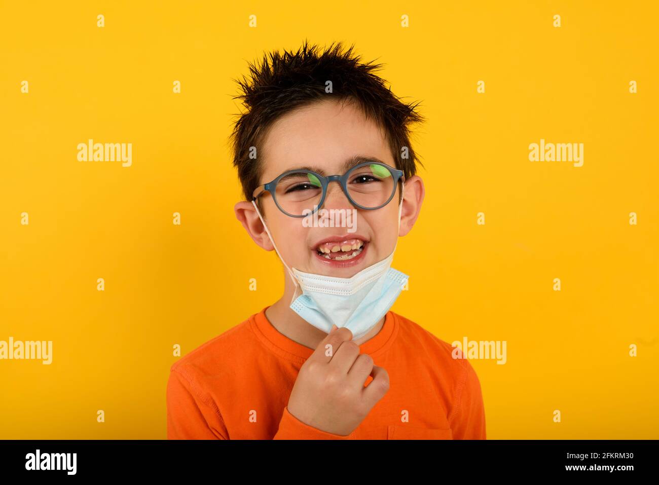 Il bambino è felice di rimuovere la maschera facciale per covid-19coronavirus. Sfondo giallo Foto Stock