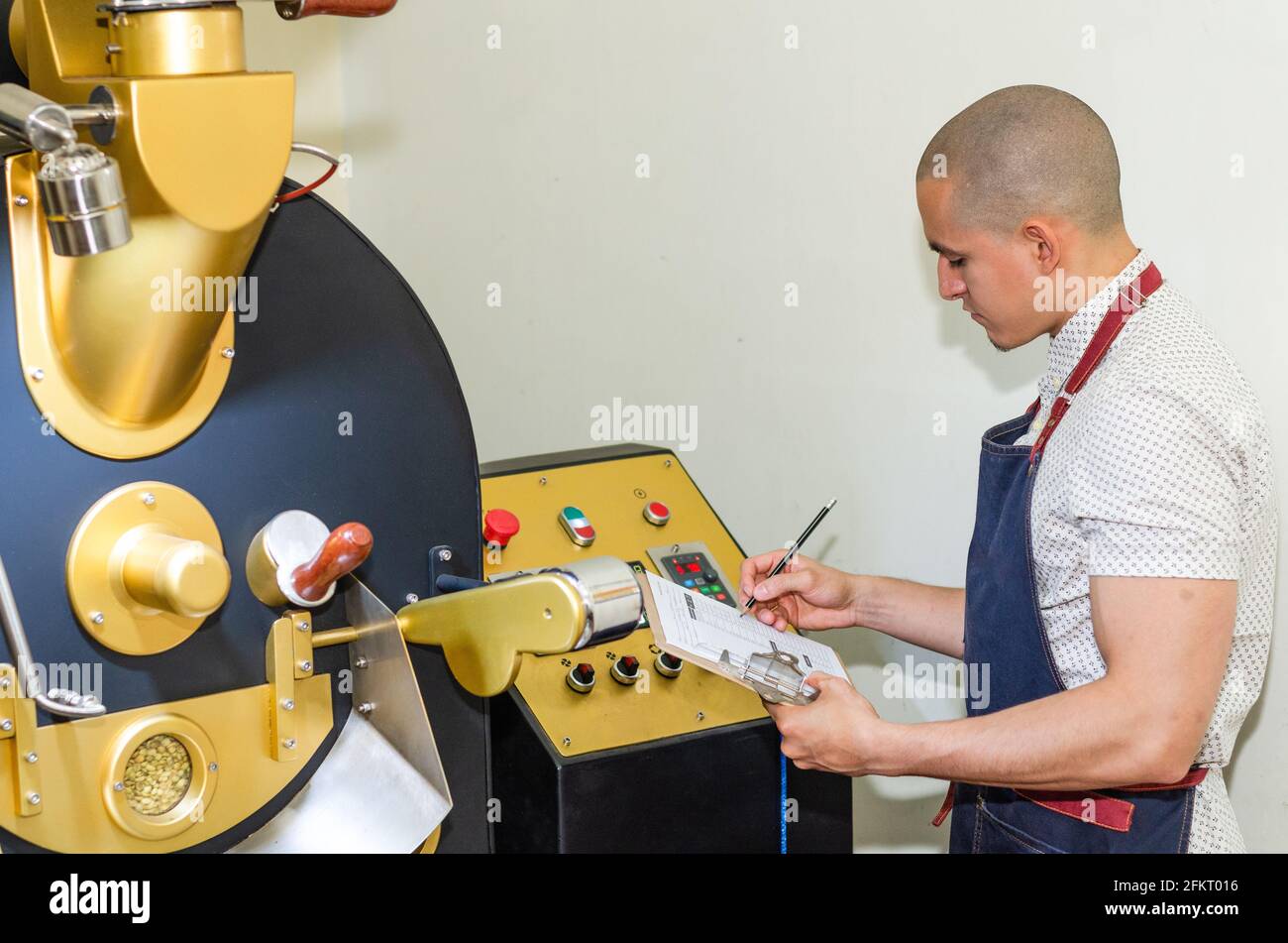 Le mani dell'uomo arrostire i chicchi di caffè aromatico su una moderna macchina utilizzata per tostare i chicchi. Foto Stock