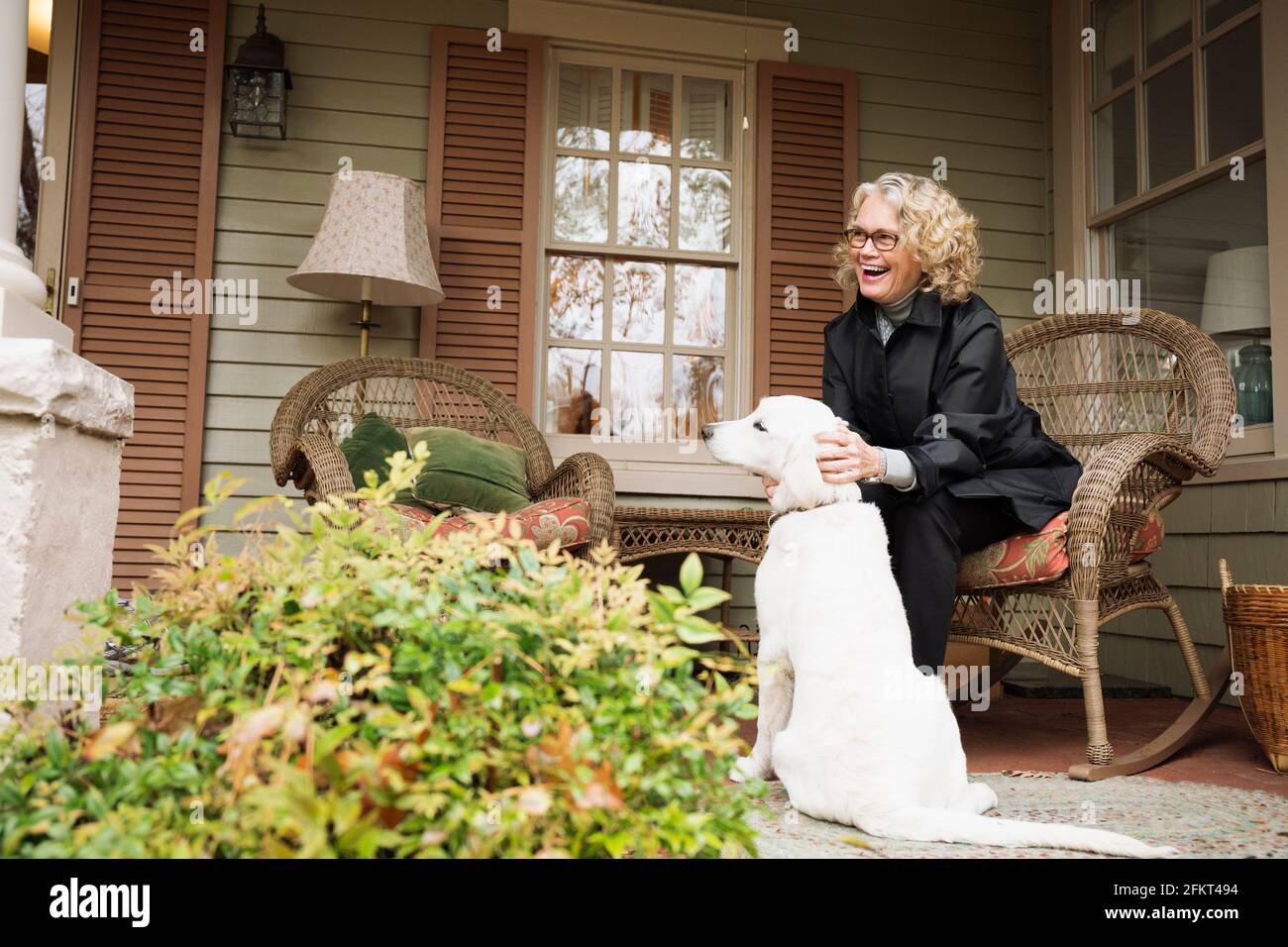 Senior donna seduta sul portico sedia a dondolo con il cane Foto Stock