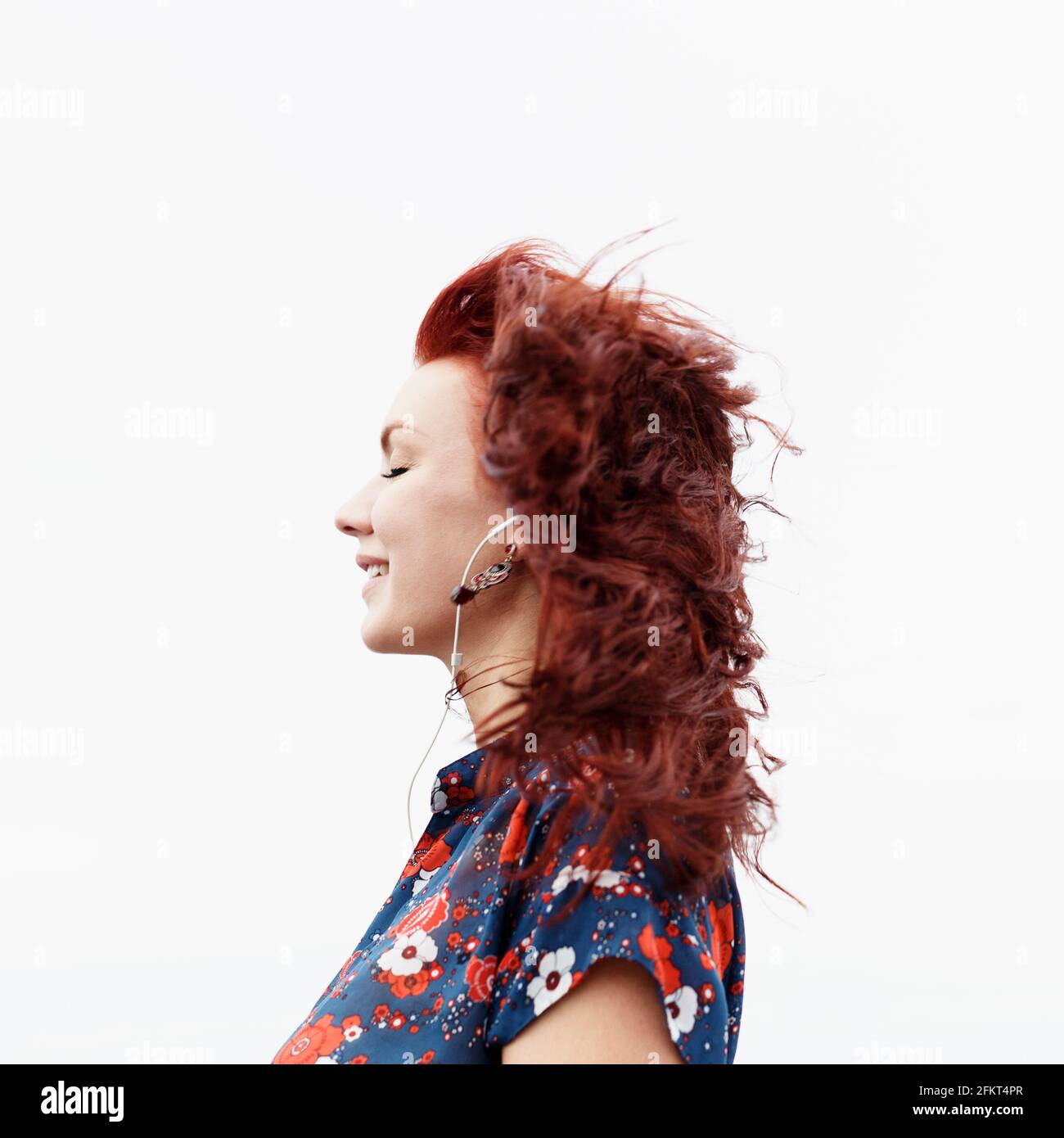 Profilo di giovane donna con lunghi capelli rossi, indossa gli auricolari Foto Stock