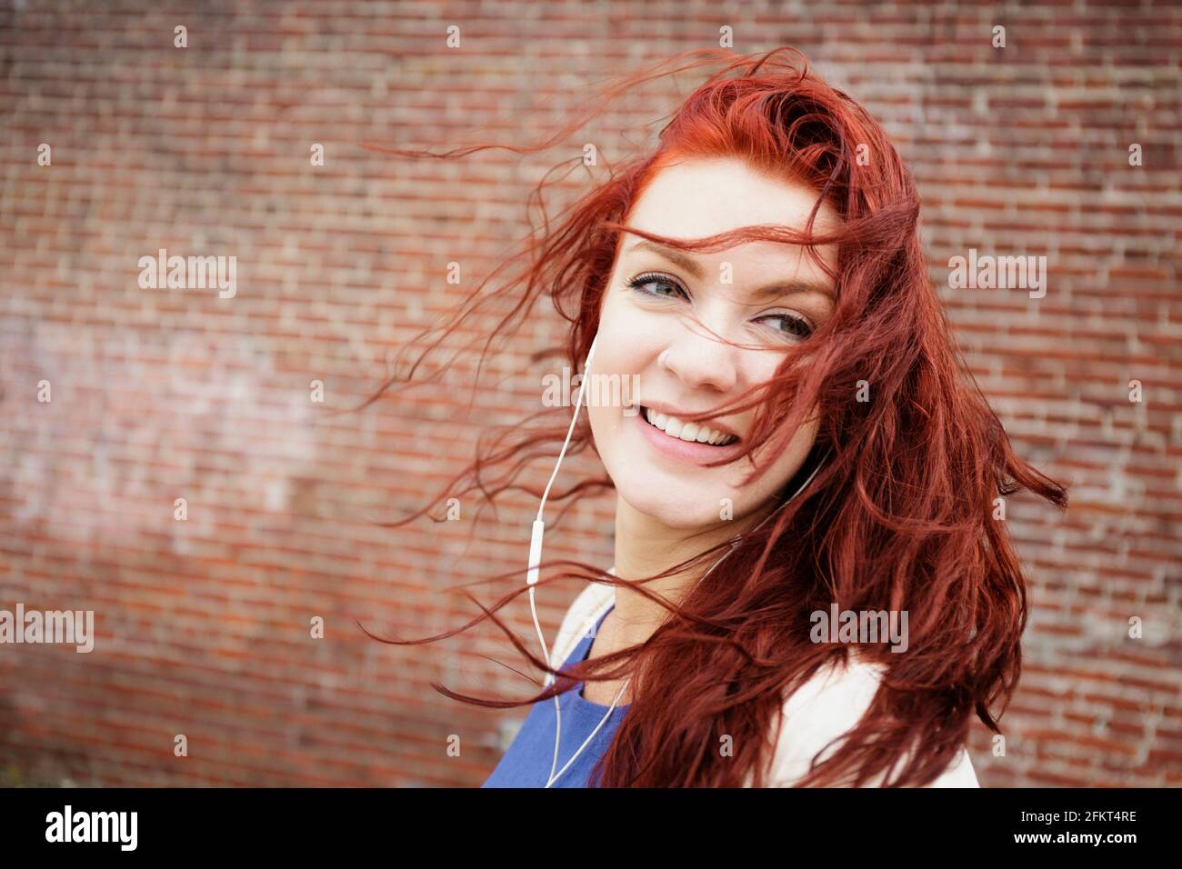 Giovane donna con lunghi capelli rossi, indossa gli auricolari, close-up Foto Stock