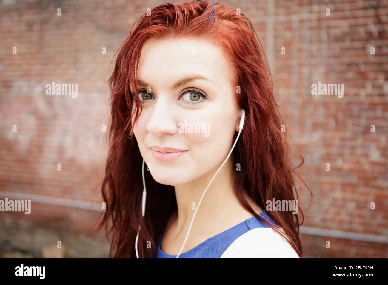 Ritratto di giovane donna con lunghi capelli rossi, indossa gli auricolari, close-up Foto Stock