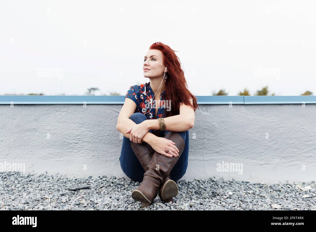 Ritratto di giovane donna seduta sul tetto, indossa gli auricolari Foto Stock