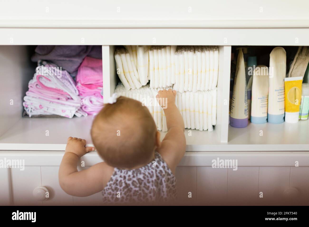 Vista posteriore della bambina di raggiungere per pannolino in armadio Foto Stock