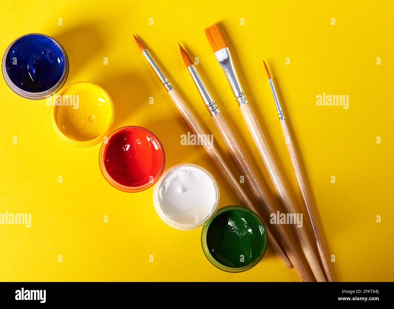 pennelli e gouache colorate si erigono su sfondo giallo Foto Stock