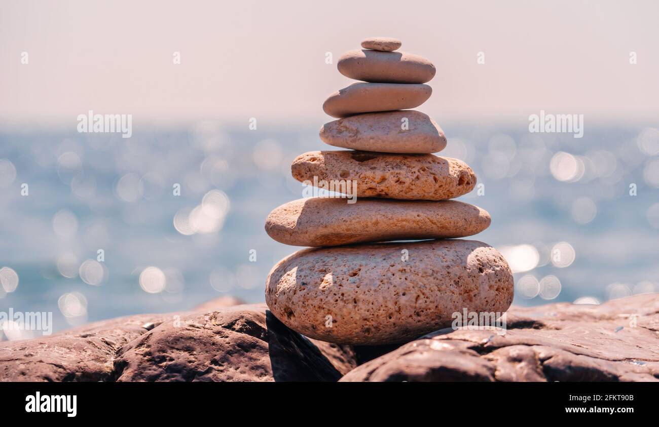 Equilibrata piramide di ciottoli sulla spiaggia in una giornata di sole. Abstract Sea bokeh sullo sfondo. Messa a fuoco selettiva. Pietre Zen sulla spiaggia di mare, meditazione Foto Stock