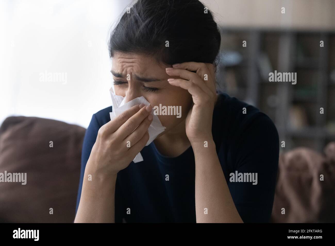 Primo piano infelice malata donna indiana che soffia naso, prendere freddo Foto Stock