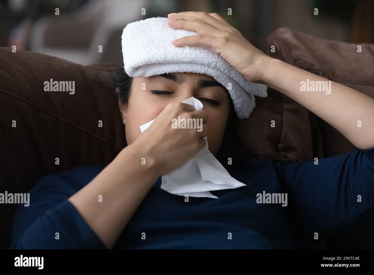 Primo piano malata donna indiana che soffia il naso, seduto sul divano Foto Stock