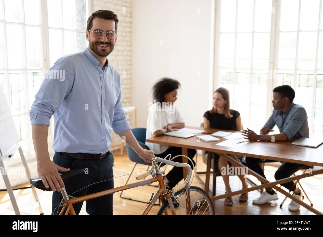 Felice giovane manager in occhiali che tiene in bicicletta, guardando la macchina fotografica. Foto Stock