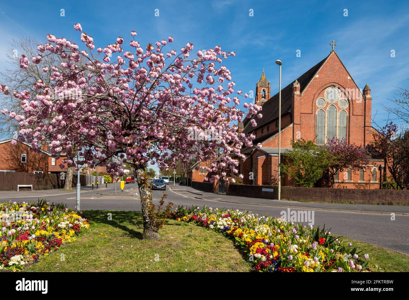 Chiesa di San Marco a Farnborough, Hampshire, Regno Unito, durante la primavera con alberi di ciliegio e aiuole colorate. Foto Stock