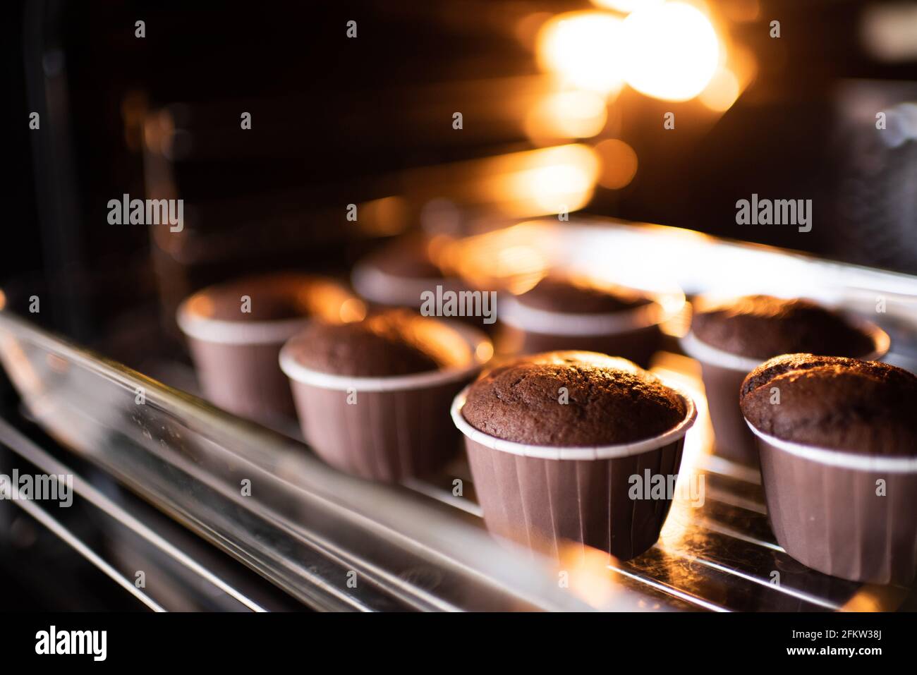 Forno a casa con gustosi muffin al cioccolato in forma di panificazione su vassoio a casa. Fare cupcakes fresco in piano cottura da vicino. Foto Stock