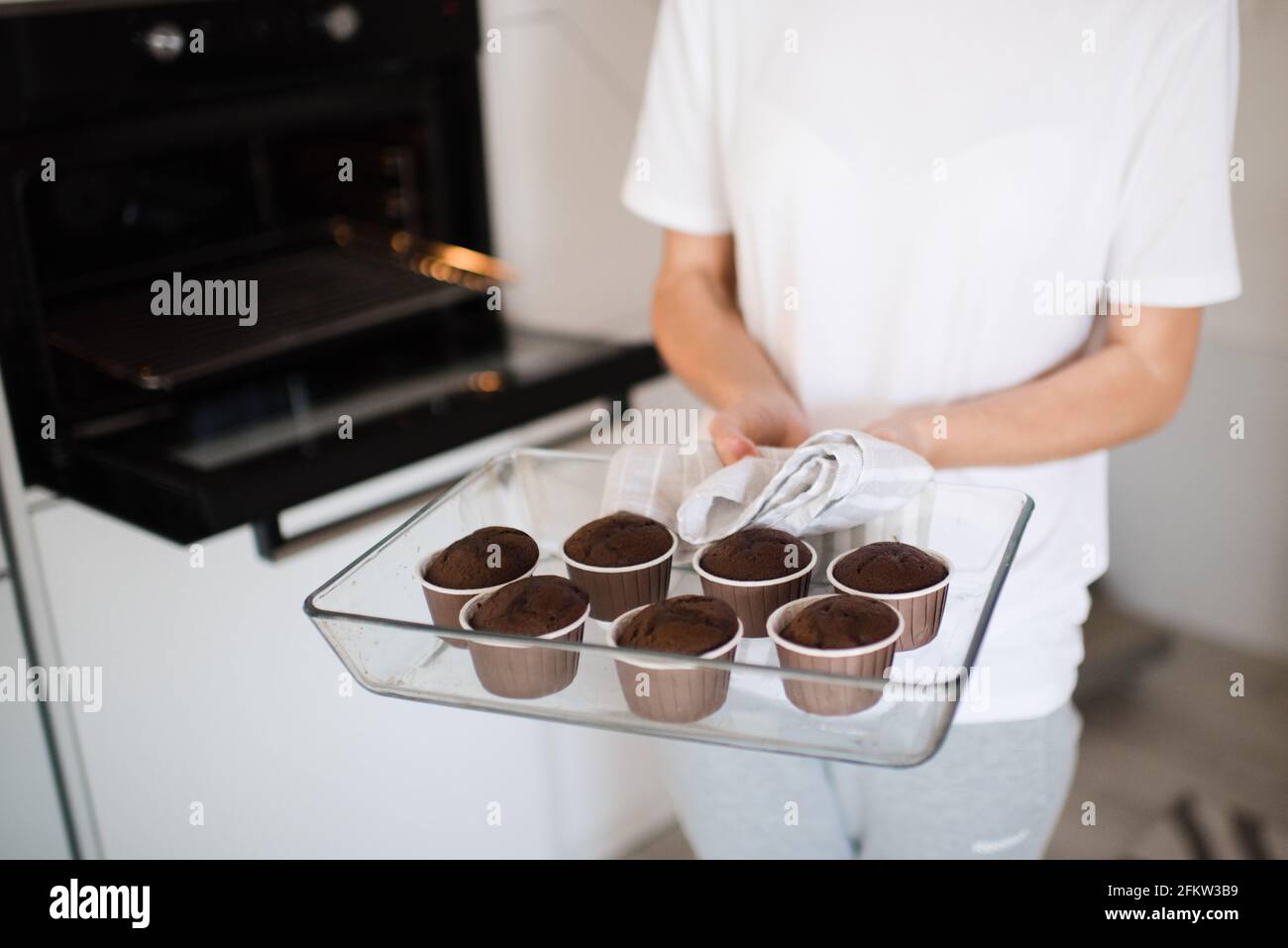 Donna con vassoio in vetro e muffin al cioccolato al forno in cucina. Forno fresco. Casalinga cuoco a casa. Foto Stock