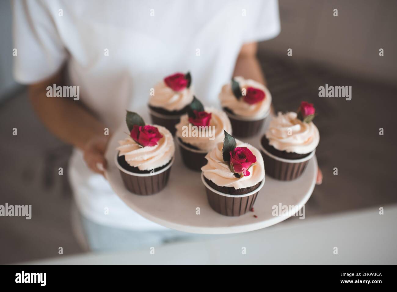 Torta della tazza della torta della donna con la glassa montata della crema e decorazione del fiore in cucina a casa primo piano. Celebrazione. Foto Stock
