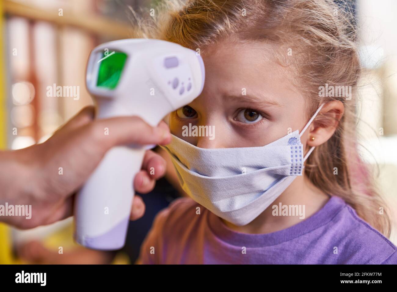 Termometro per fronte con supporto manuale per la misurazione della febbre senza contatto in una ragazza in asilo Foto Stock