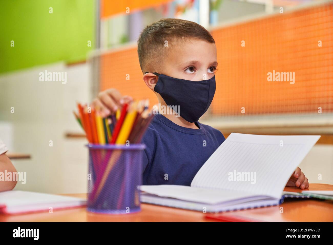 Ragazzo con maschera a causa di Covid-19 come studente in classe in scuola prescolare o elementare Foto Stock