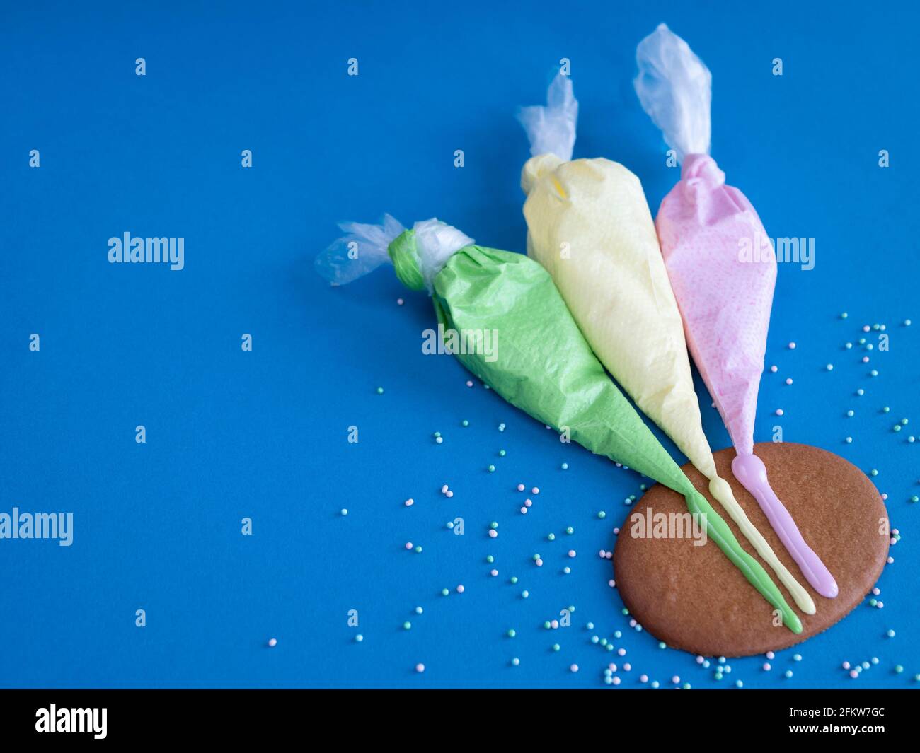 Tre sacchetti di piping con glassa colorata per la decorazione dei biscotti sullo sfondo blu, spazio di copia Foto Stock