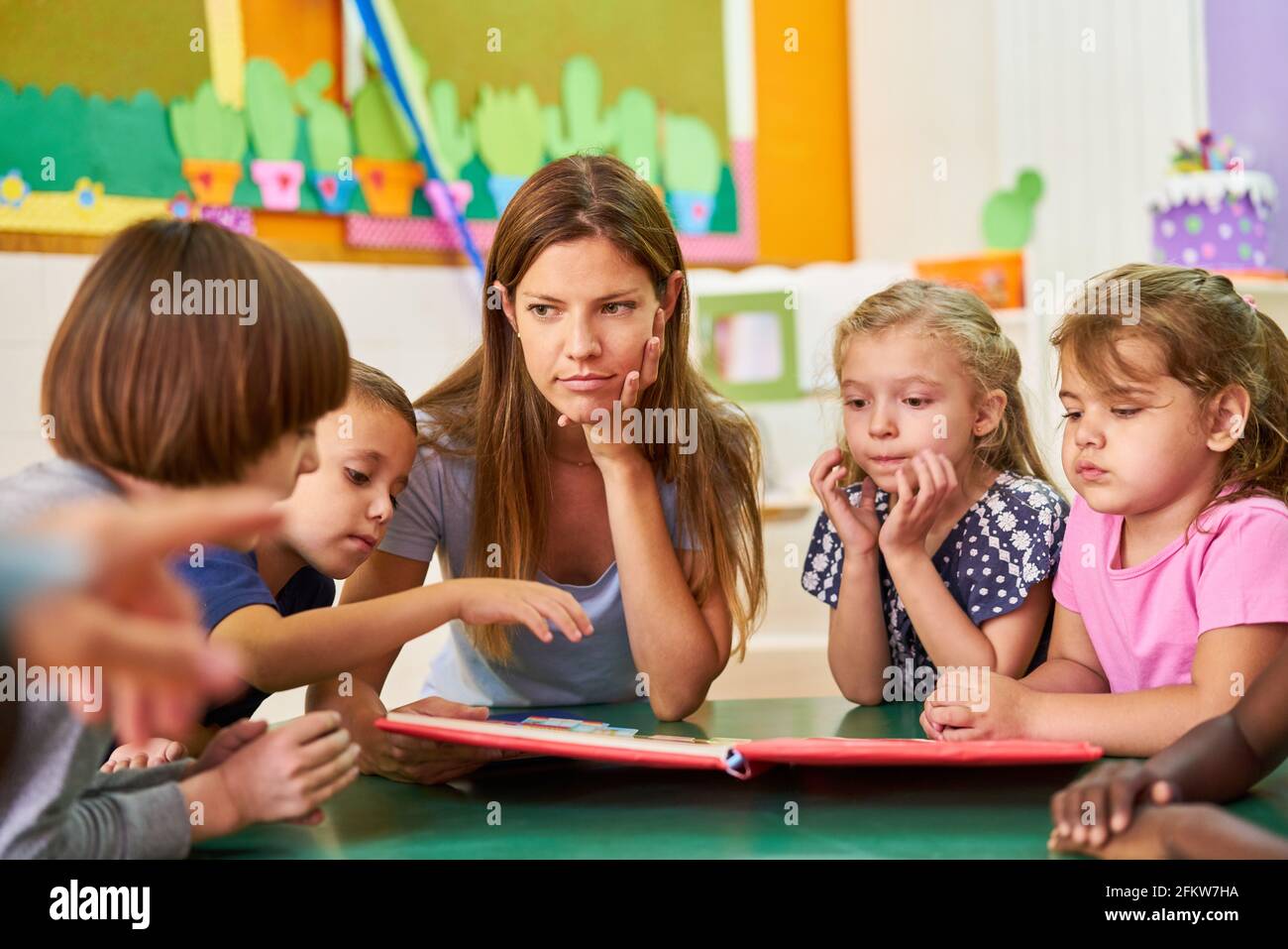 Gruppo di bambini e caregiviere di leggere insieme in un bambino prenota in asilo nido Foto Stock