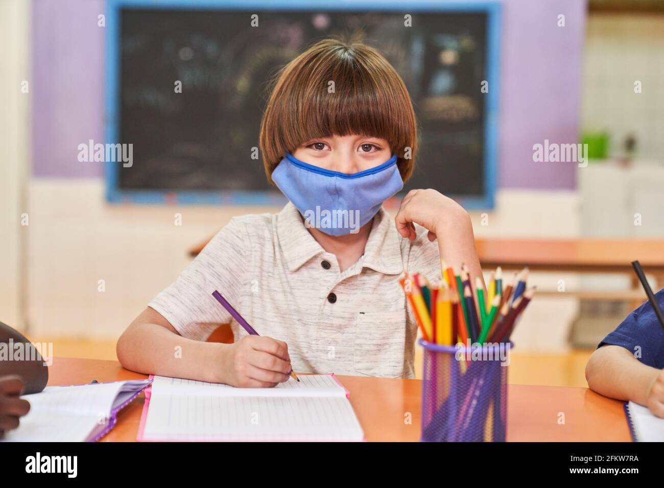 Bambino con maschera a causa di Covid-19 e Coronavirus durante lo studio in scuola elementare o prescolare Foto Stock