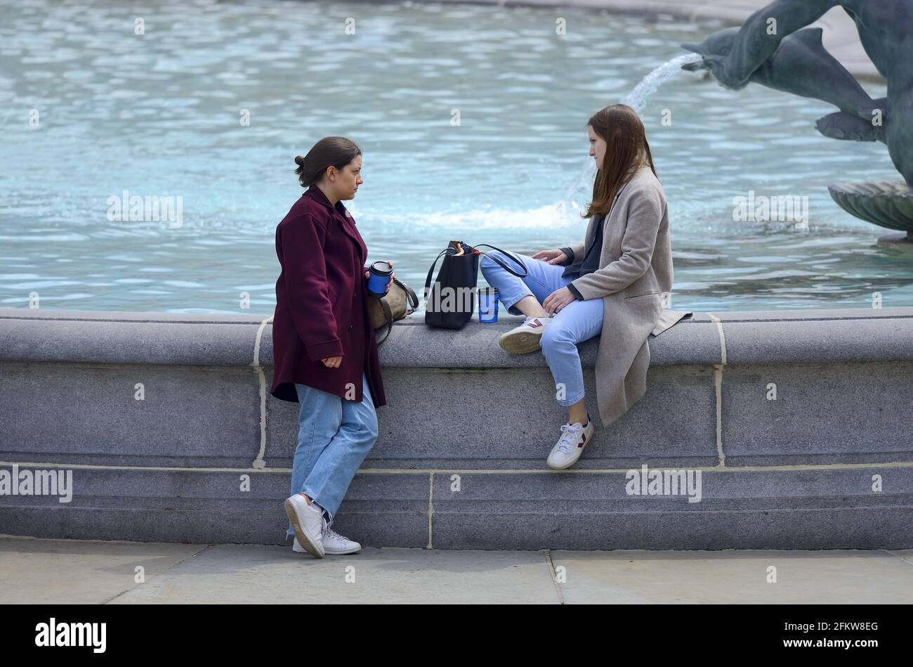 Londra, Inghilterra, Regno Unito. Due giovani donne che parlano presso la fontana in Piazza Trafalgar Foto Stock