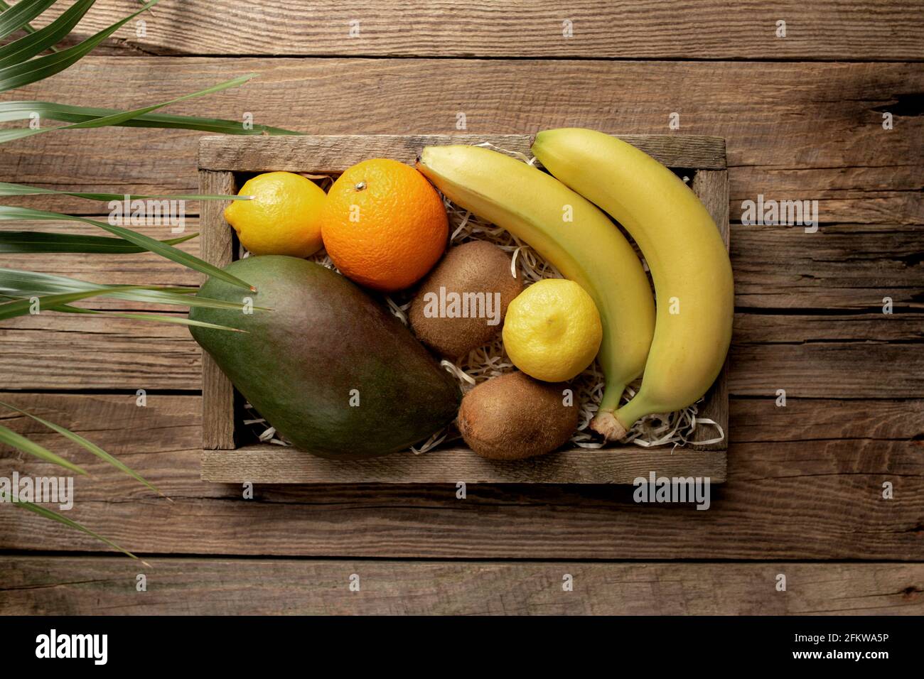 Frutta tropicale fresca in una scatola di consegna di legno su sfondo di legno. Arancione, banana, mango, kiwi e limone vista dall'alto piatto con spazio per la copia per som Foto Stock