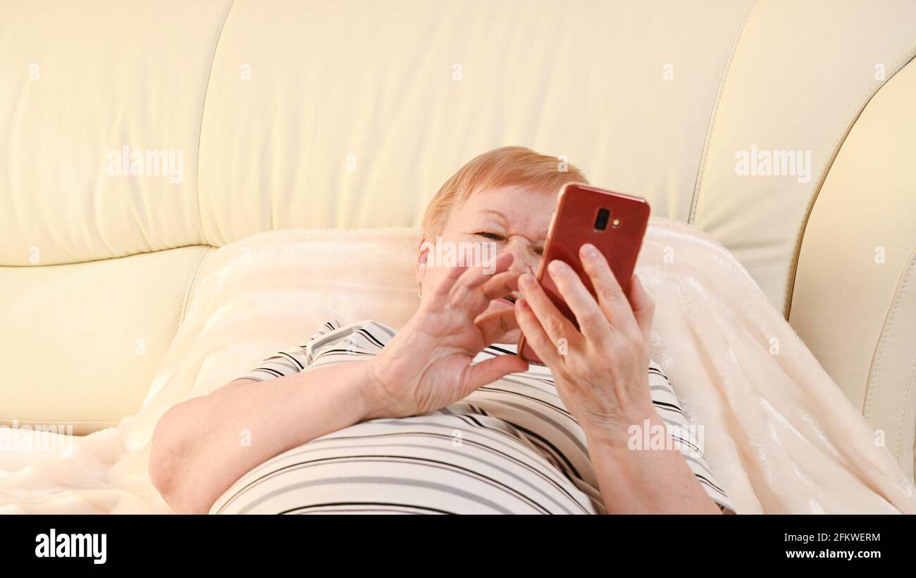 Una donna anziana si trova nella camera da letto con un telefono nelle sue mani Foto Stock