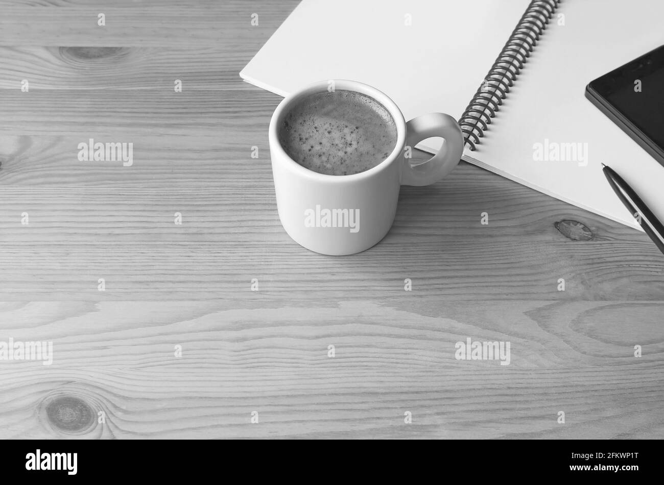 Tazza di caffè caldo con una nota e un cellulare acceso Scrivania in legno monocromatico Foto Stock