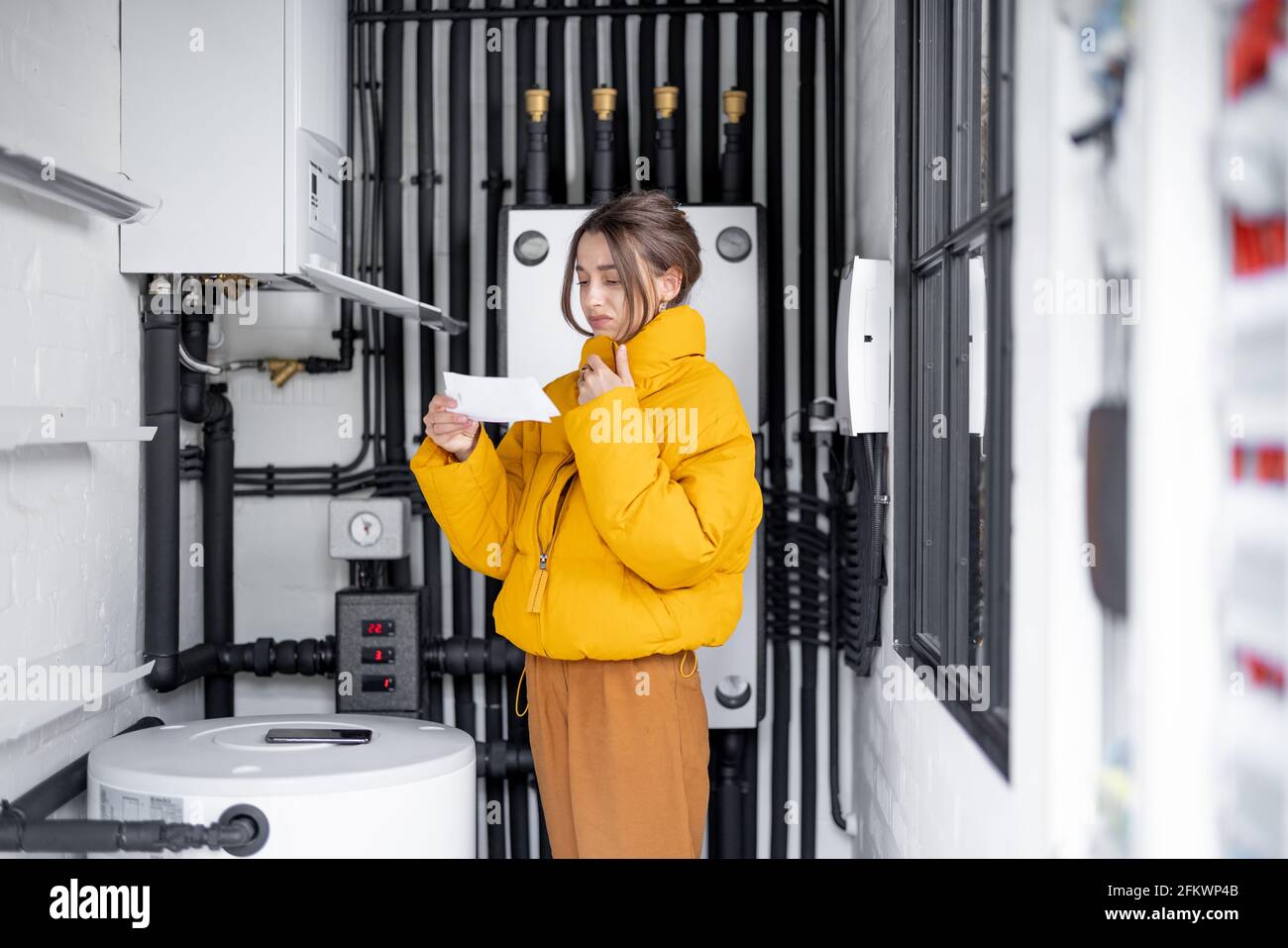 Donna confusa guarda le bollette elettriche, confrontando i dati con il misuratore nel quadro elettrico a casa. Concetto di spese per la famiglia Foto Stock