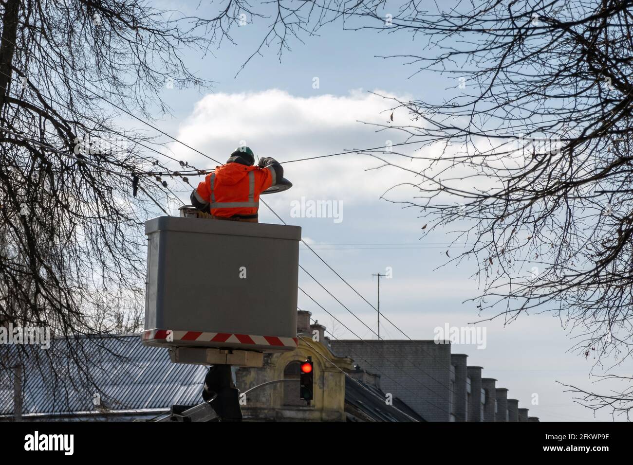 Elettricista in una piattaforma di ascensore che indossa abiti da lavoro protettivi cambiando le luci di strada in una giornata di sole. Foto Stock