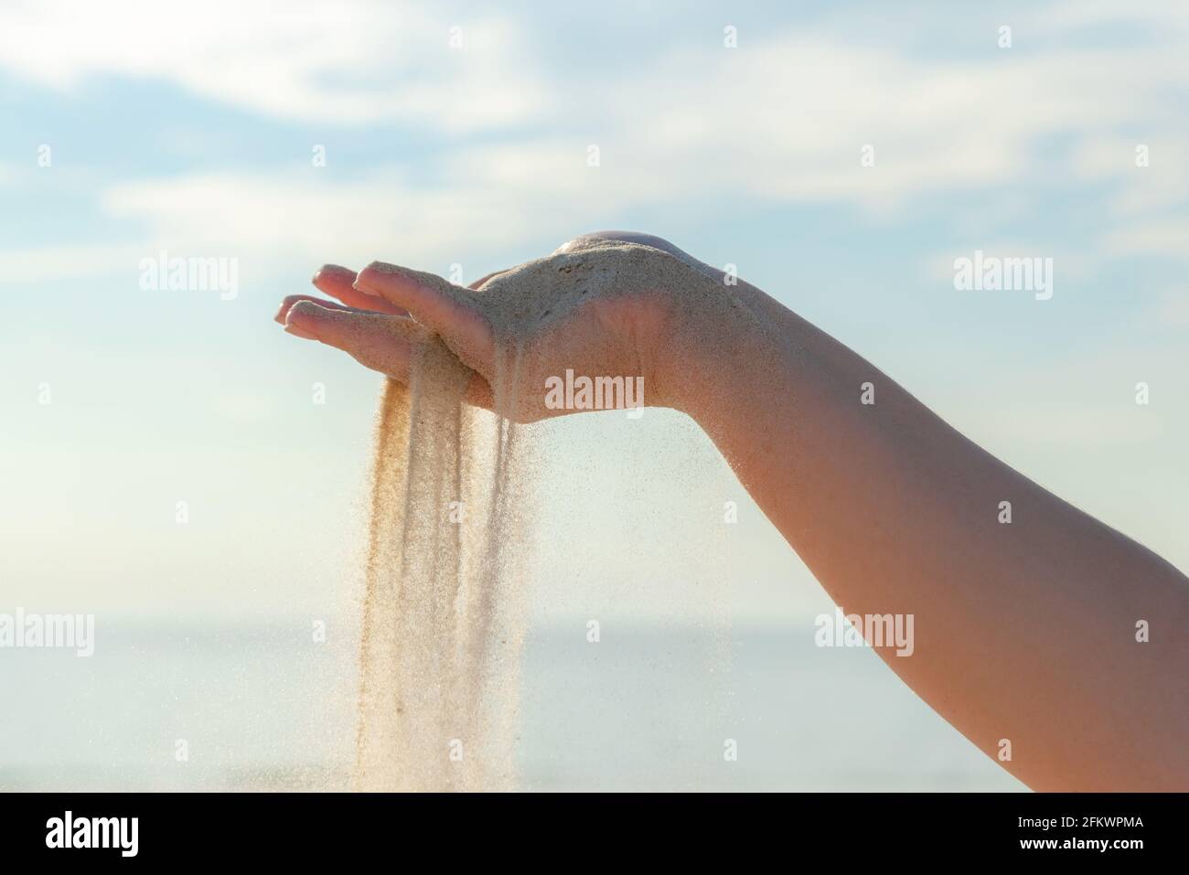 Primo piano di sabbia che si riversano dalla mano sulla spiaggia in una soleggiata giornata estiva. Giocare con la sabbia in vacanza. Foto Stock