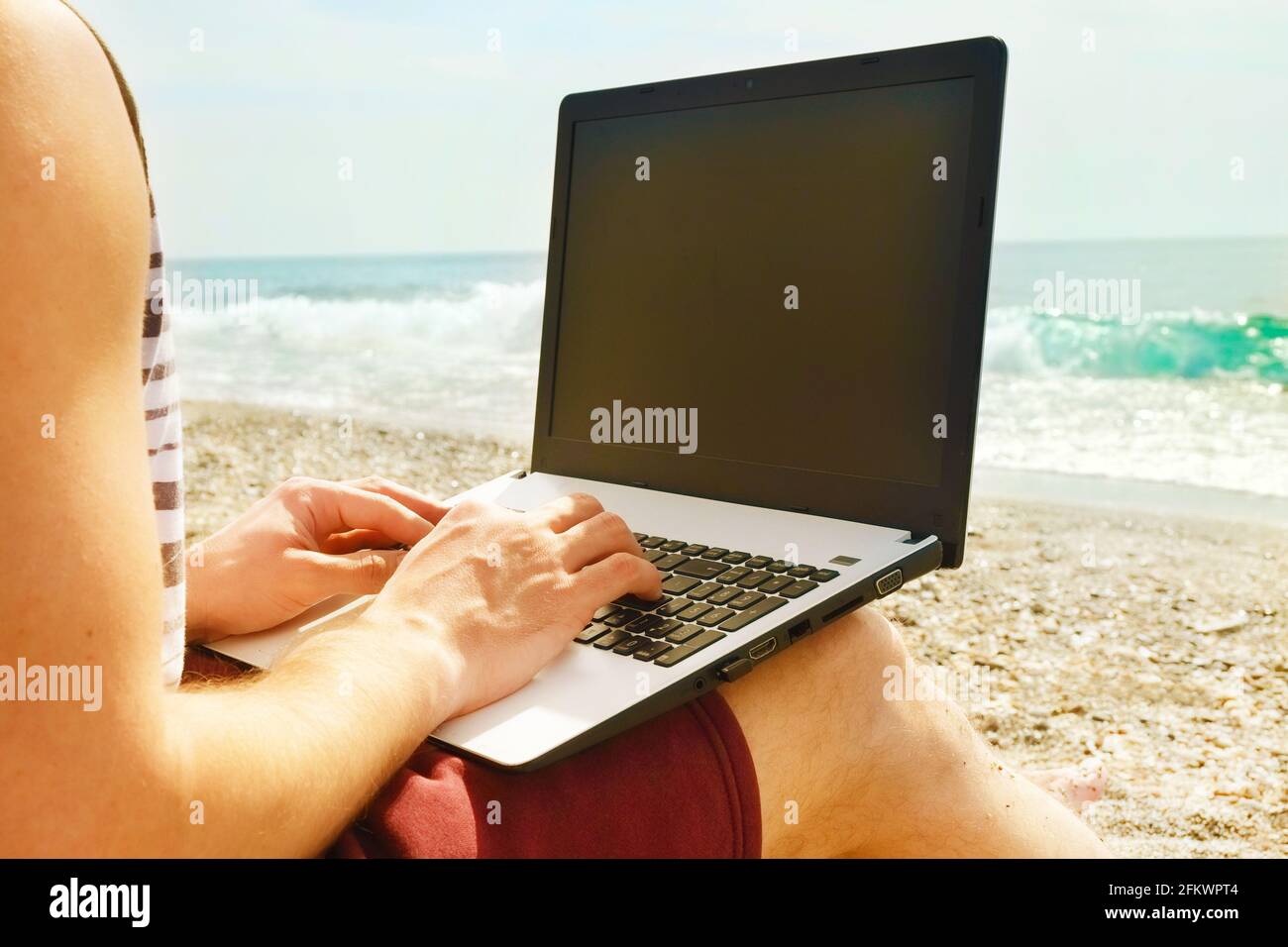 Programmatore muscolare FIT giovane uomo seduto sulla spiaggia di sabbia, computer portatile, schermo vuoto, blogging di codifica, navigazione. Concetto di lavoro a distanza per freelance. Se Foto Stock