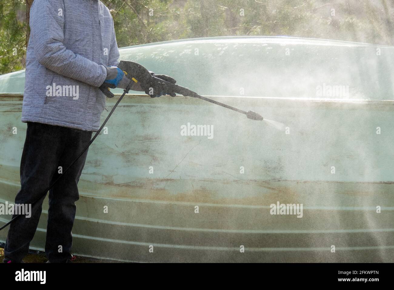 Primo piano della mano con guanti che spruzzano acqua compressa per pulire lo sporco della superficie esterna dell'imbarcazione. Manutenzione della barca a vela. Foto Stock