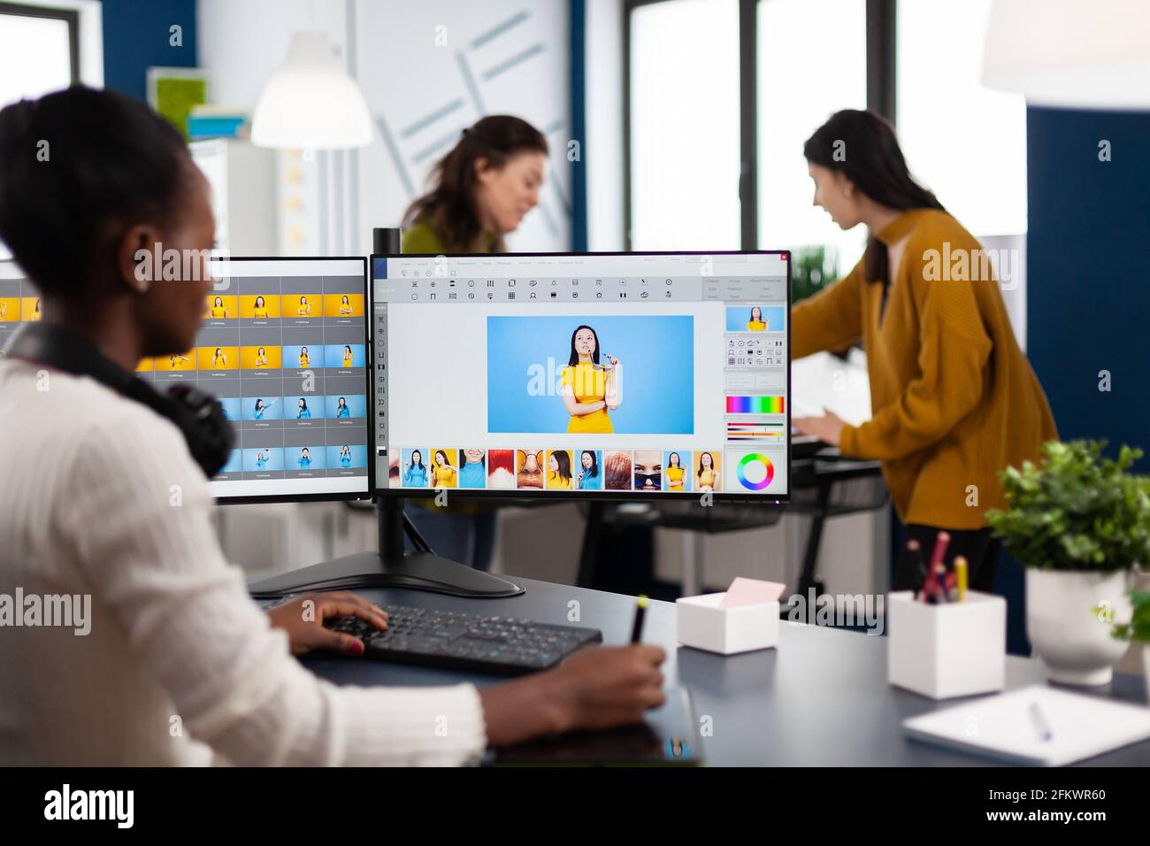 Donna africana retoucher seduta in moderno studio creativo di foto che lavora sul computer dopo il photoshoot, ritocco di fotografie di modello in software di editing di immagini con stilo matita, colore ingrassare app. Foto Stock