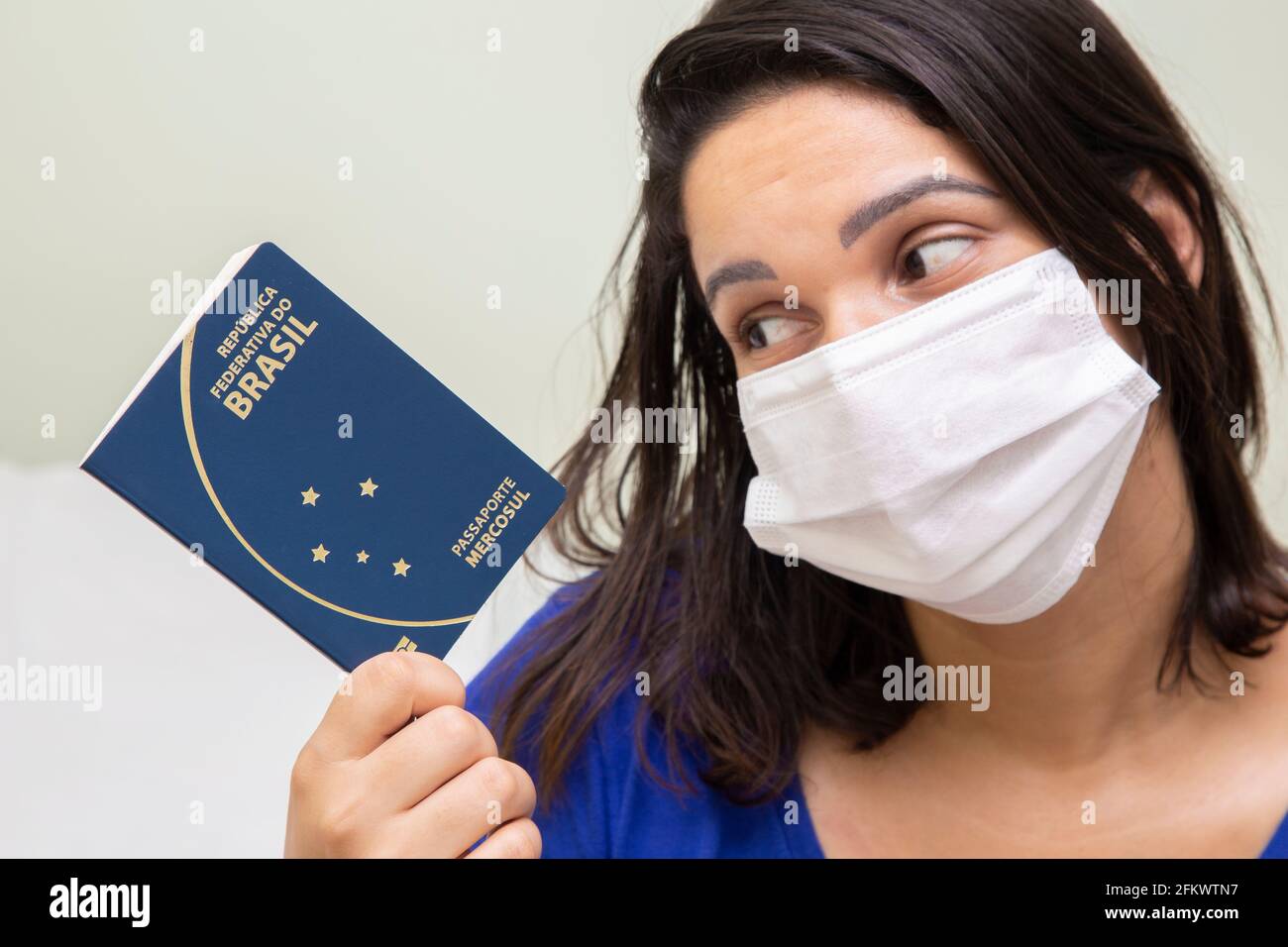 Donna mascherata con passaporto brasiliano in mano. Foto Stock