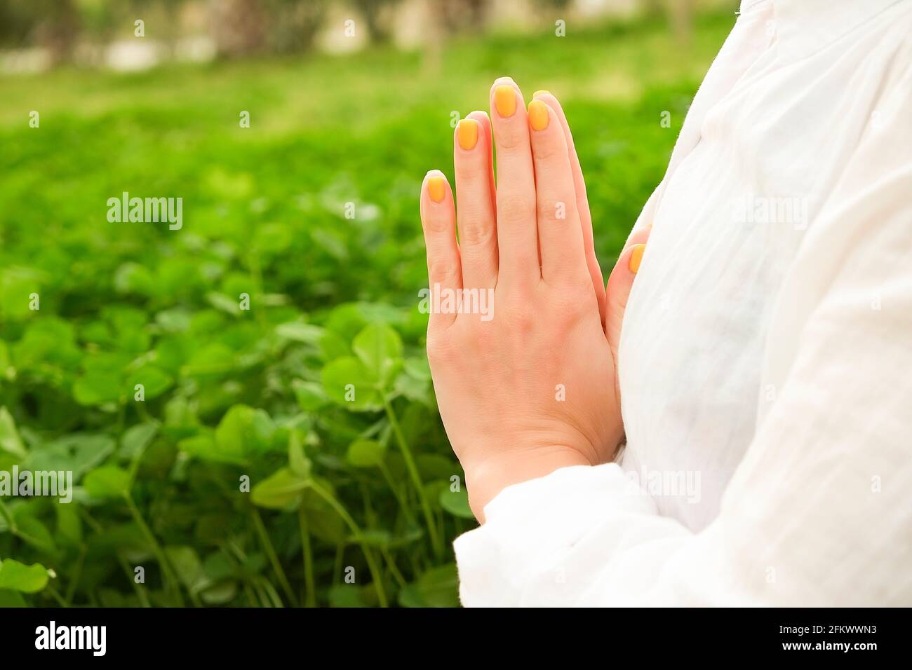 Irriconoscibile giovane donna che pratica yoga, seduta in posa di namaste Padmasana Lotus. Donna sportiva, camicia in cotone oversize che medita all'aperto, erba f Foto Stock