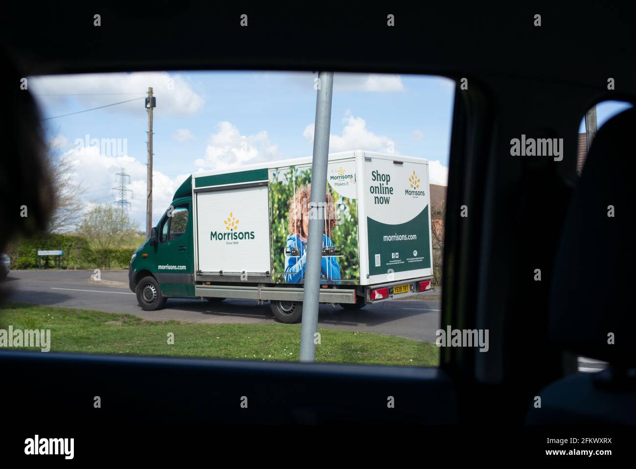 Acquista online il pulmino Morrisons visto dal punto di vista di un passeggero in un'auto che viaggia lungo una strada del villaggio. Foto Stock