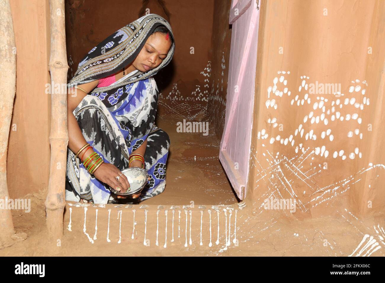 Donna sposata che fa la pittura tradizionale usando la pasta di riso all'entrata della sua casa a Kuanarpal villaggio di Cuttack distretto di Odisha, India Foto Stock