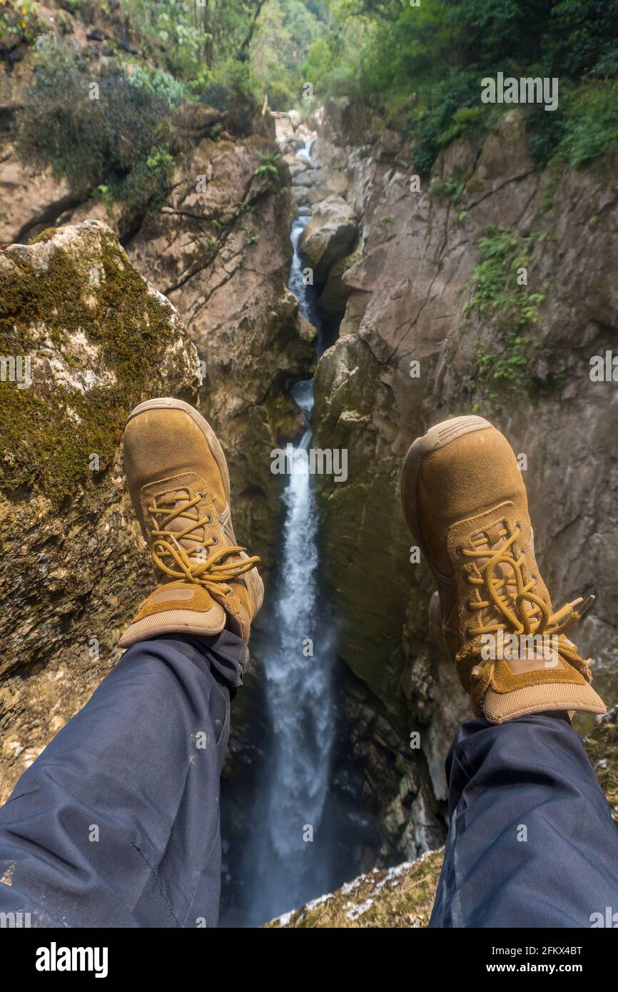 Immagine verticale di una gamba di escursionisti ispanici che penzolano con una vista sulla cascata Foto Stock