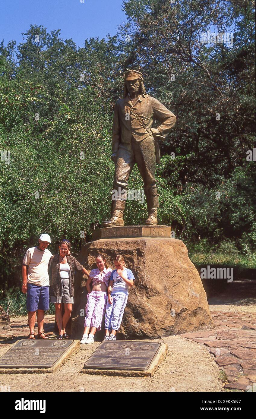 Famiglia in posa della statua commemorativa di David Livingston (esploratore vittoriano) alle Cascate Vittoria, Cascate Vittoria, Matabeleland, Zimbabwe Foto Stock