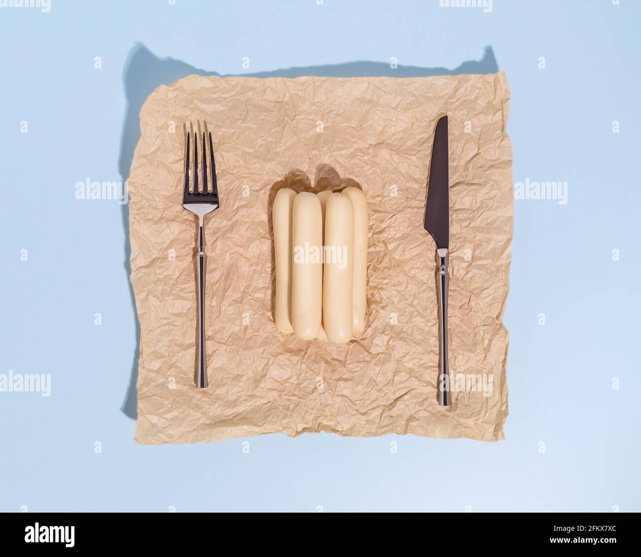 Composizione alimentare orizzontale con salsicce di pollame su carta da imballaggio con un coltello e una forchetta su sfondo blu. Integratori alimentari sani di carne prod Foto Stock