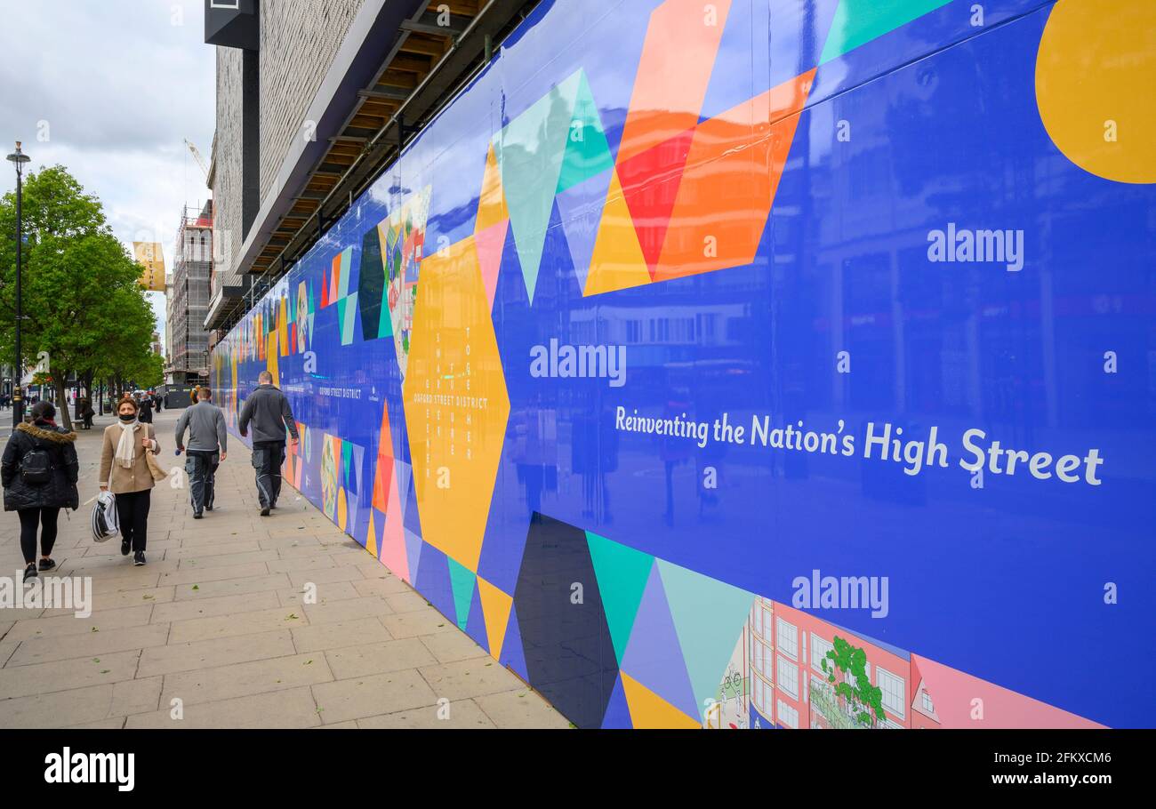 Lo shopper che indossa il facemask passa accanto al colorato livello della strada che nasconde l'ex negozio Debenhams a Oxford Street, Londra, 4 maggio 2021 Foto Stock