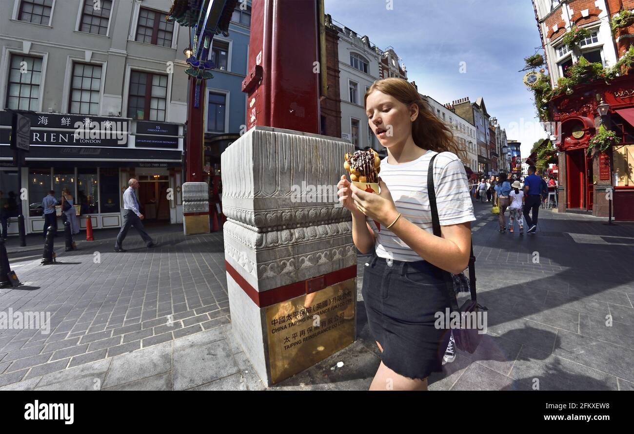 Londra, Inghilterra, Regno Unito. Giovane donna con waffle alle uova e gelato a Wardour Street, Chinatown Foto Stock