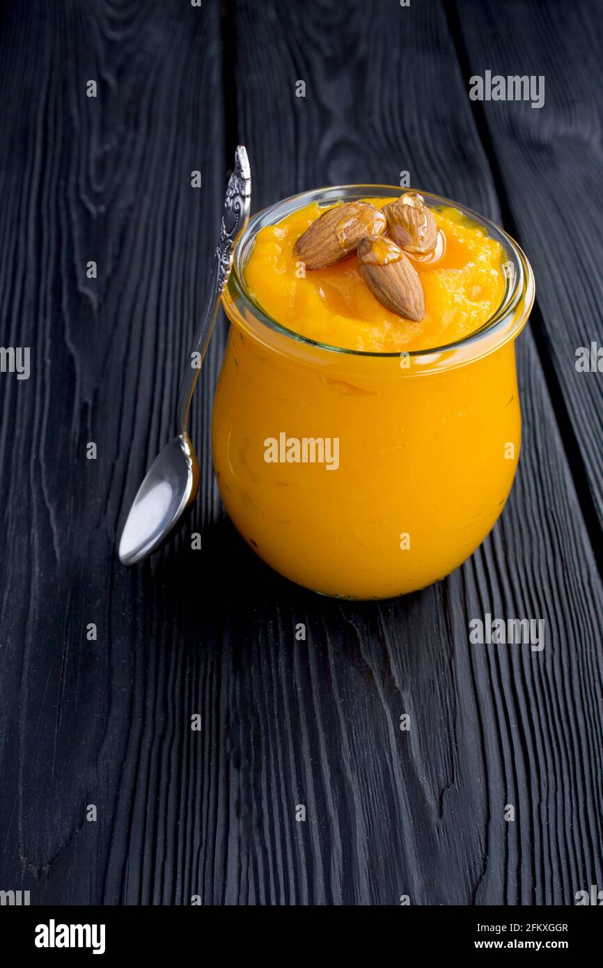 Purea con zucca, mandorle e miele nel vaso di vetro sullo sfondo nero di legno. Spazio di copia. Posizione verticale. Foto Stock