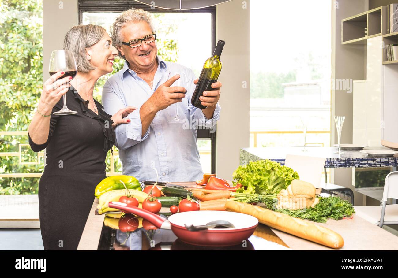 Coppia anziana che cucinano cibo sano e bevendo vino rosso a. Casa cucina - pensionati a casa preparare il pranzo con verdure fresche e bio produ Foto Stock