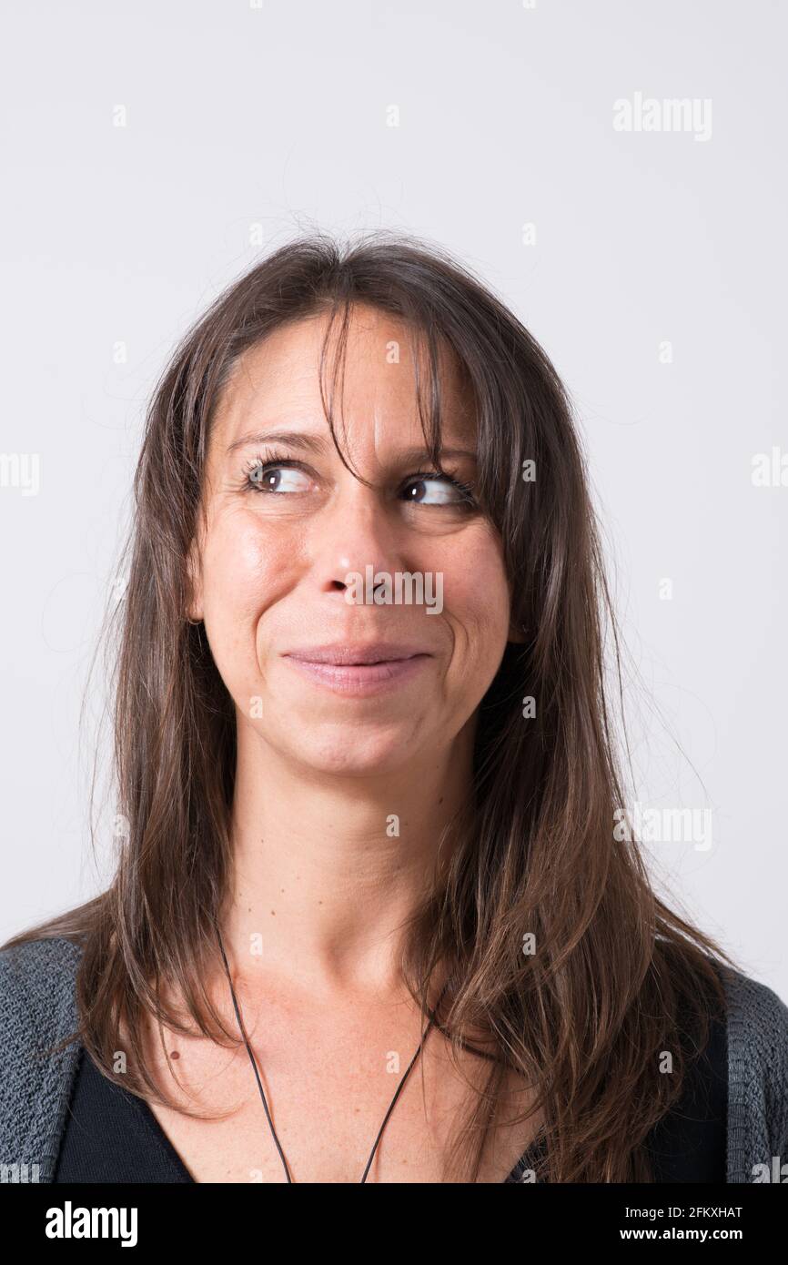 Headshot di una donna mediterranea di 30-40 anni con una faccia divertente alla macchina fotografica che guarda alla sua destra. Sfondo bianco Foto Stock